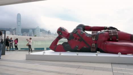 locals and tourists flock to an 8-meter deadpool installation in hong kong, taking photos against the skyline. the display promotes disney's "deadpool and wolverine" movie.