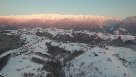 Toma-Aérea-De-Las-Montañas-Piatra-Craiului-Al-Amanecer-Con-Un-Pueblo-Cubierto-De-Nieve