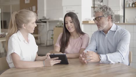 young pretty blonde woman showing something on tablet to other people on a cafeteria