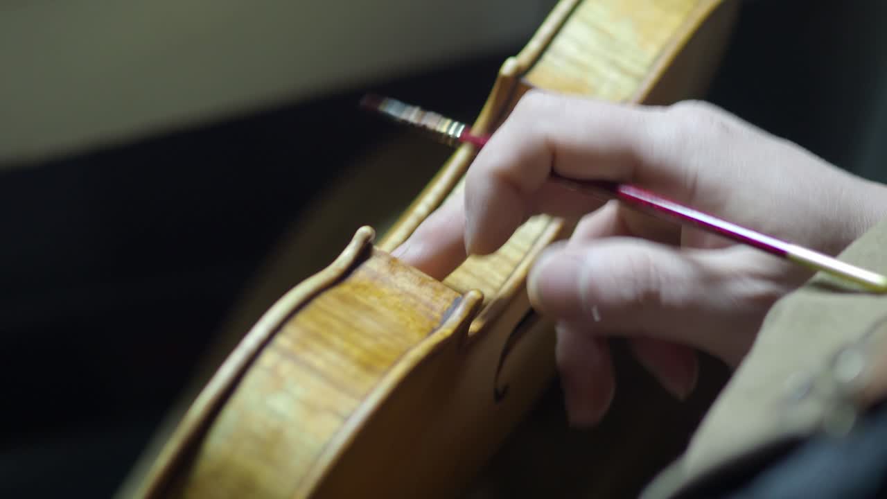 Close-up of a luthier using artist-grade Brown Madder Alizarin oil glaze, brushed and finger-rubbed across a violin’s surface to achieve a nuanced, antique effect with subtle color variation