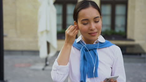 cheerful woman dancing and listening music walking towards the camera outdoors