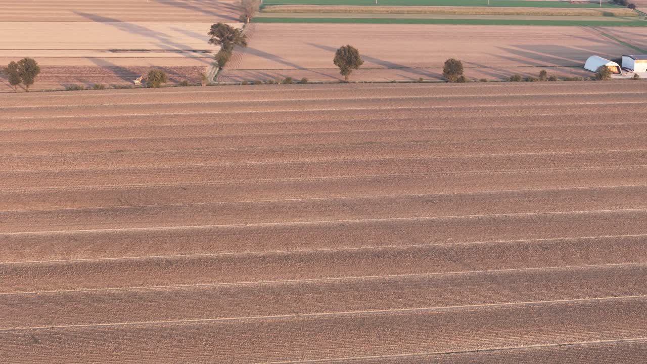 Drone image of a recently tilled field in the Po Valley near Piacenza, Italy, with parallel furrows, farm buildings, and late-summer textures