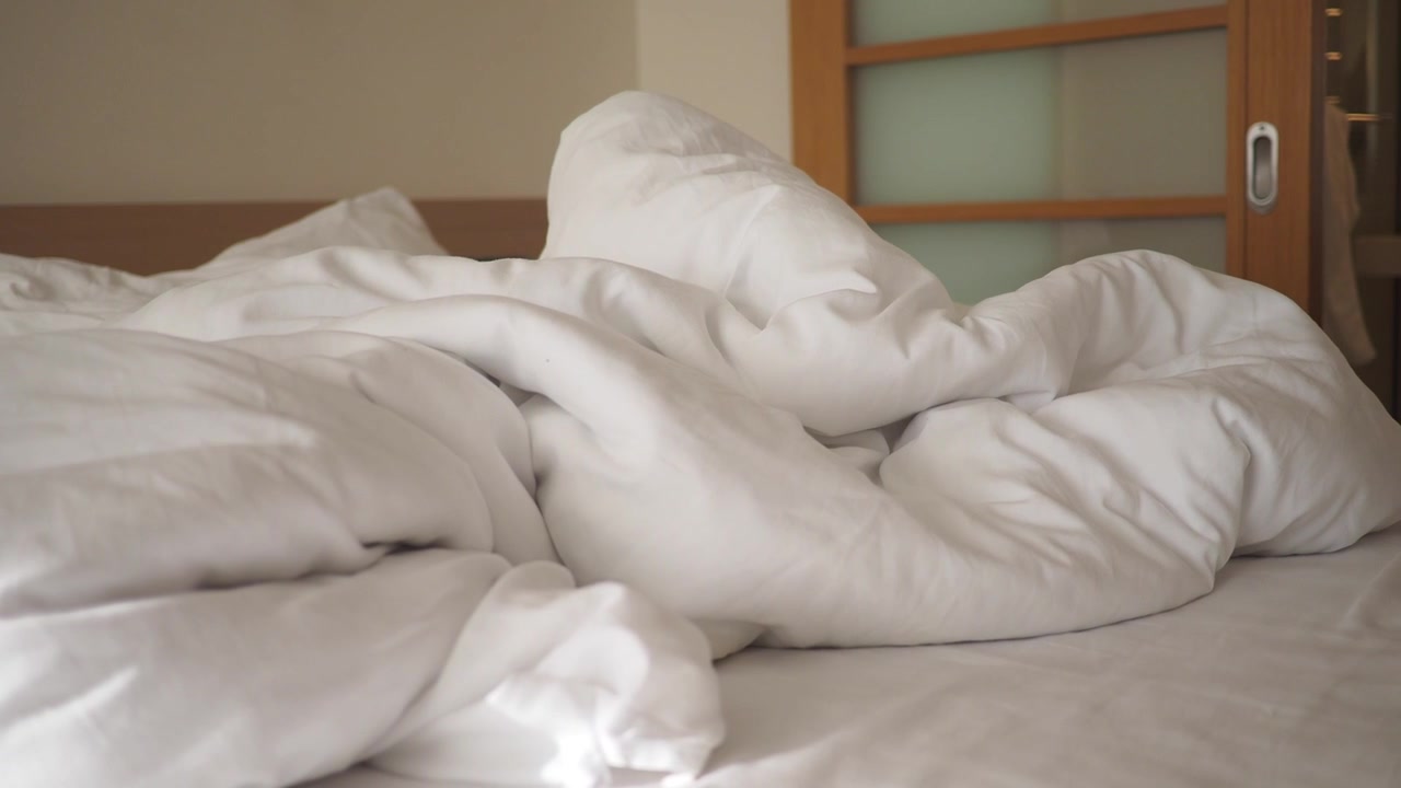 Letto sfatto con piumone bianco in una camera da letto