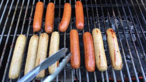 turning brats on an outdoor propane grill with thongs