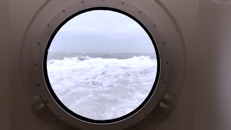 view through a porthole on a stormy sea with waves hitting the ship