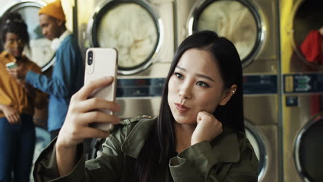 joven hermosa chica alegre sonriendo y posando para la cámara del teléfono inteligente mientras toma una foto selfie en el servicio de lavandería