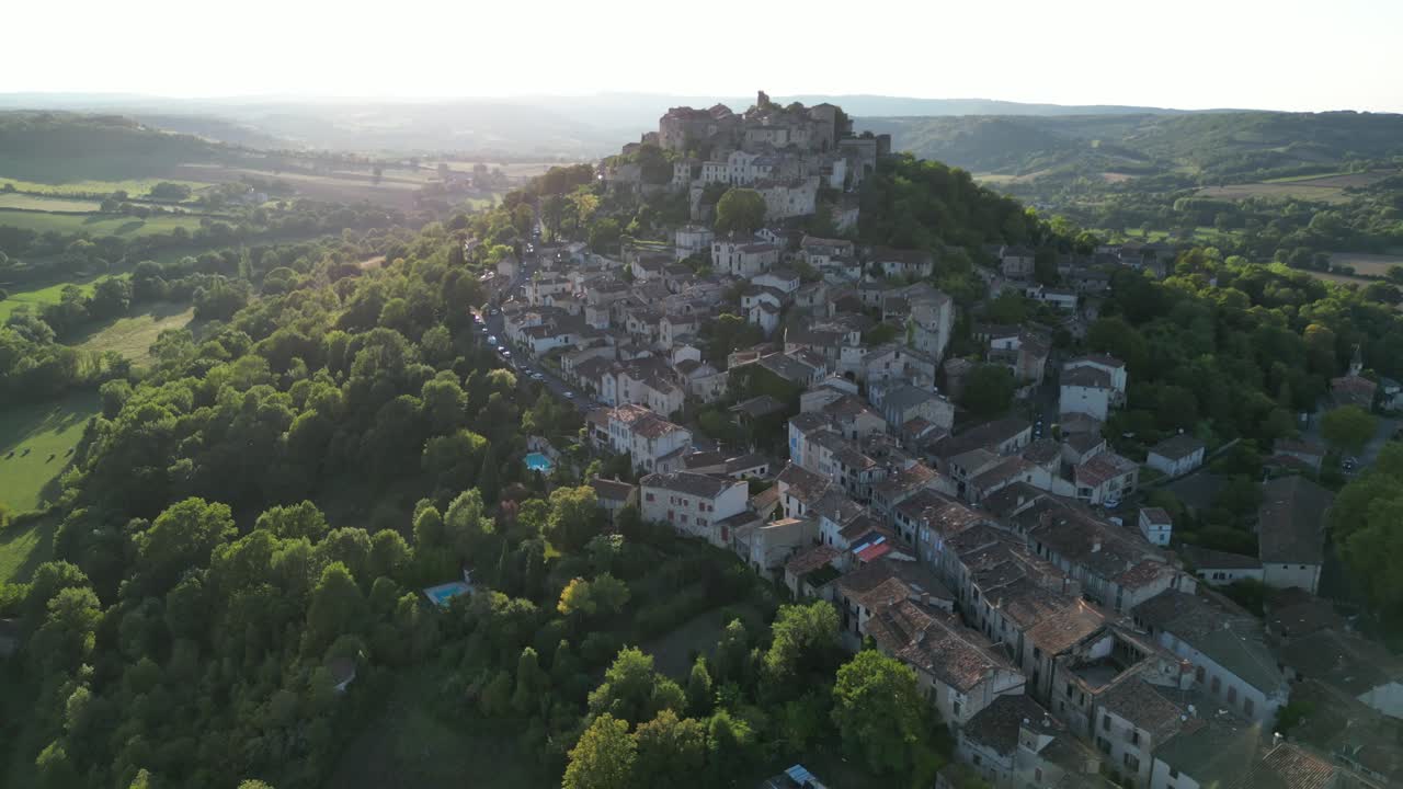 Drone aerial view in France countryside small old medieval brick town on a mountain top surrounded by green fields zooming out on a sunny day in Cordes Sur Ciel