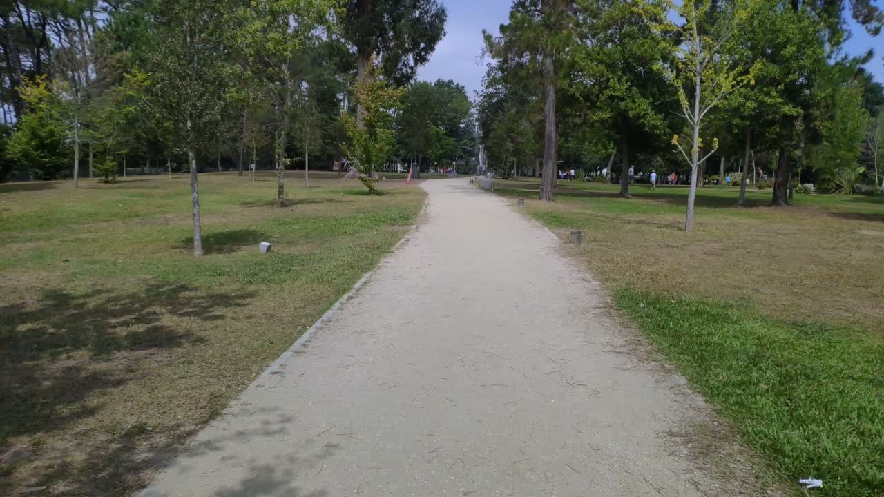 Padres con hijos disfrutando en los juegos del parque público con sus jardines y árboles en una soleada mañana de verano.