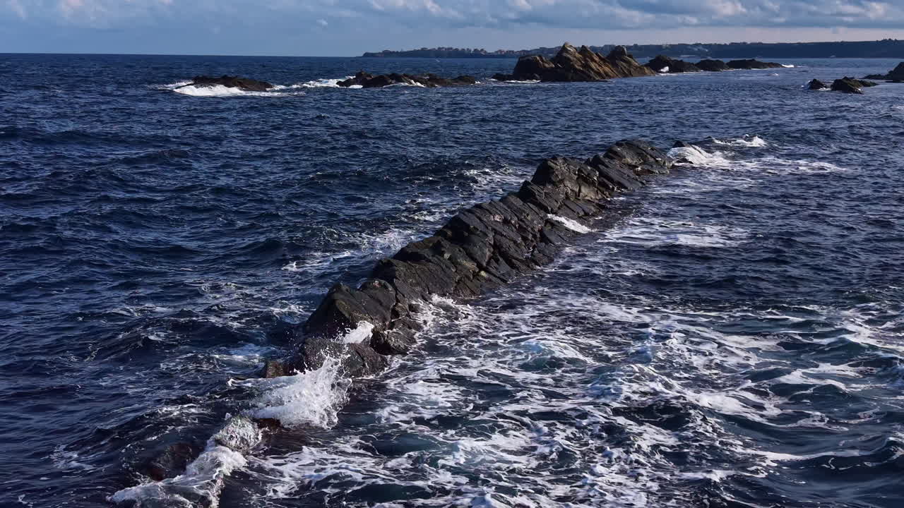 Waves crashing against rocky coastline under a bright sky at midday, revealing the beauty of nature's wild spirit