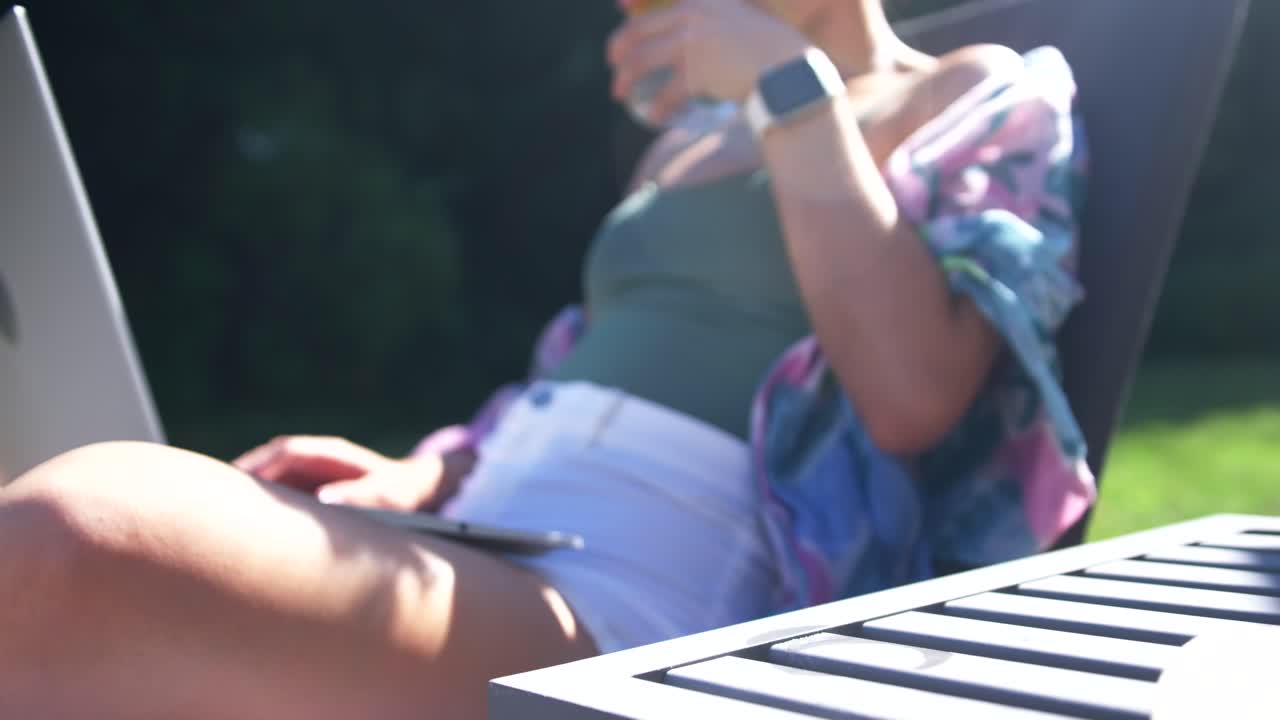 Donna adulta sdraiata su una sedia da patio, che solleva un bicchiere con limone e offre da bere, indossando un top verde