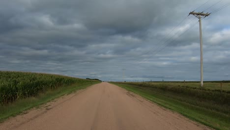 pov while driving on a rural gravel road with small seed business, fields, power lines, telephone lines and farm houses along the road