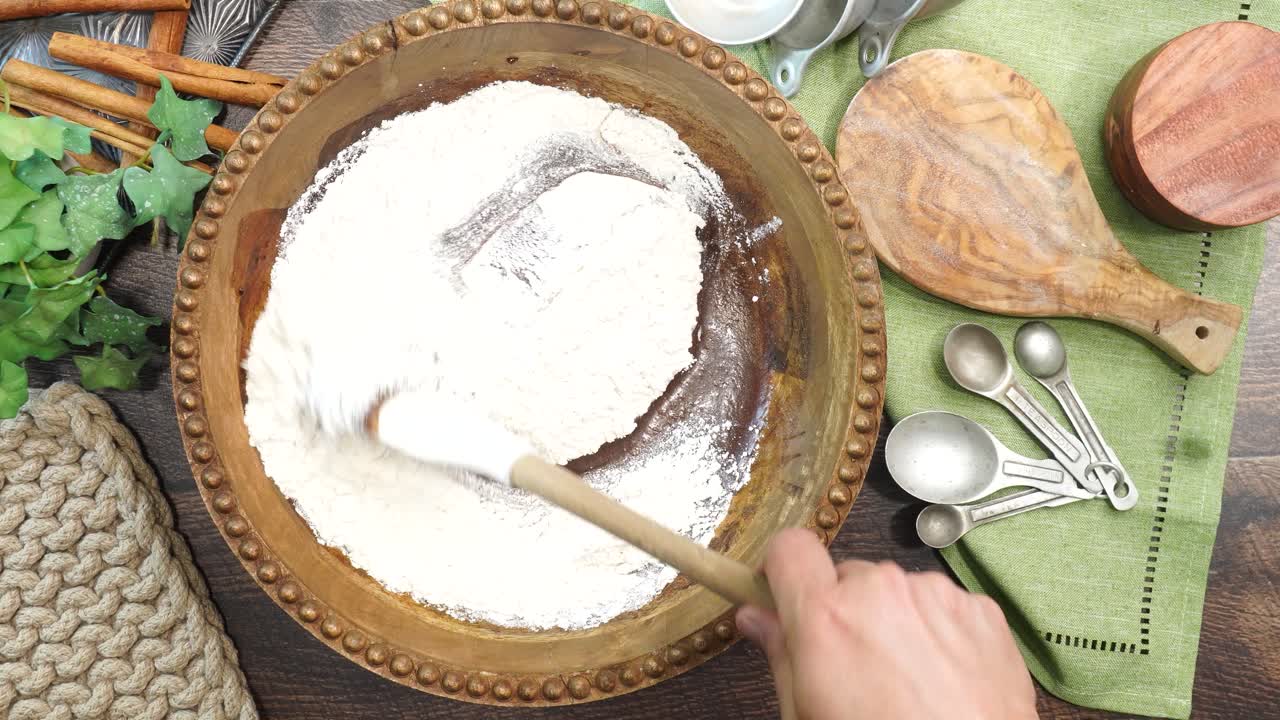 Baking a carrot cake loaf with cream cheese icing and topped with roasted salted pecans. Making a Autumn dessert with carrots, flour, sugar, nuts and frosting. Using a spatula to mix in the flour.