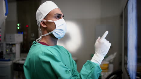 cirujano masculino biracial mirando con escáneres de rayos x en la sala de operaciones en el hospital, cámara lenta