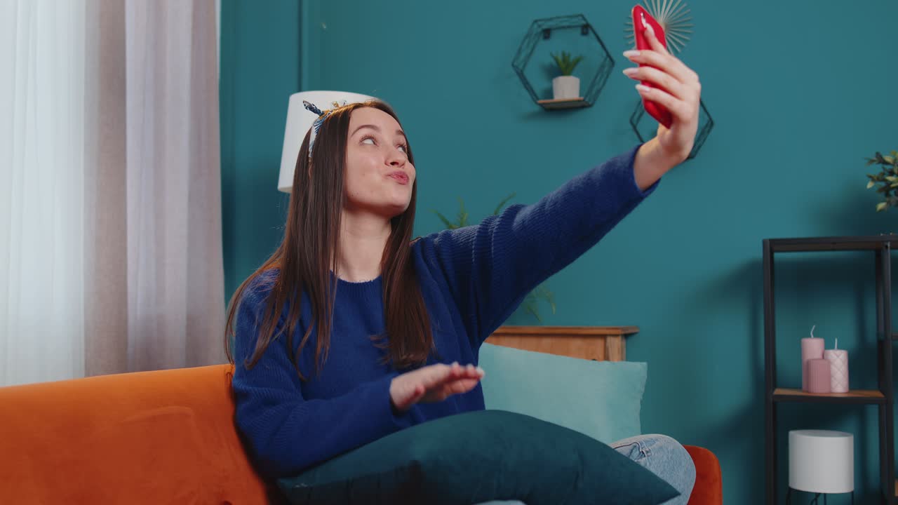 Donna sul divano a casa con lo smartphone che si fa un selfie con la fotocamera del cellulare, videochiamata virtuale online