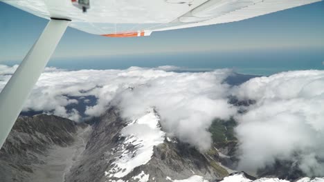 slowmo - aerial shot from plane scenic flight over west coast franz josef, aoraki mount cook, national park with clouds, snowcapped rocky mountains and ocean in background