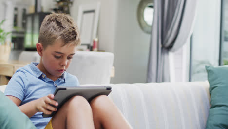feliz niño caucásico sentado en el sofá y usando la tableta, espacio de copia, cámara lenta