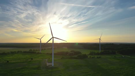 large wind turbines with blades in field aerial view bright orange sunset blue sky wind park slow motion drone turn