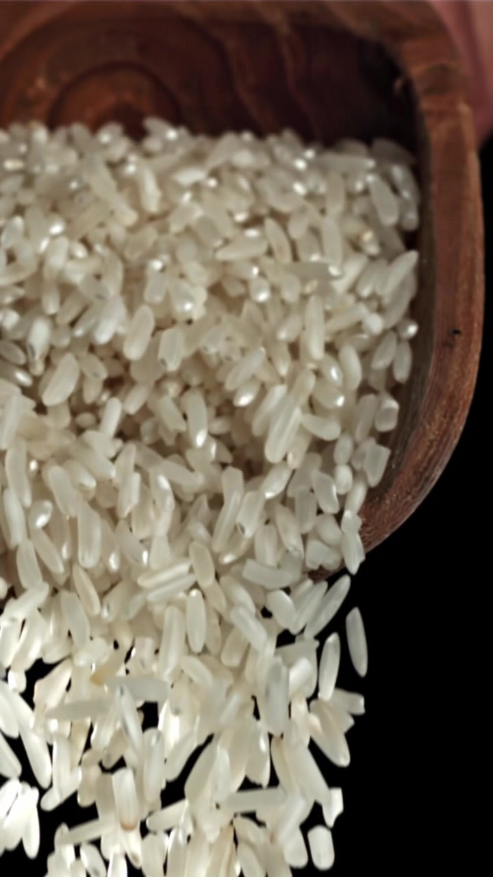 Chicchi di riso bianco che cadono da un cucchiaio di legno al rallentatore