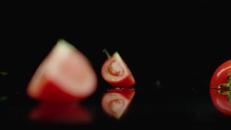 juicy sliced ​​red tomato fall into 4 parts glass with splashes of water in slow motion on a dark background