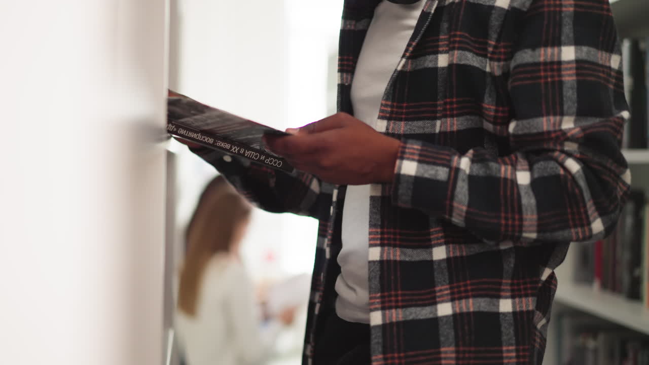 Black man holds book in university library closeup. Engrossed reader reads textbook standing near rack in bookshop. Student chooses scientific literature