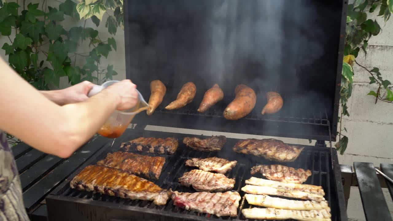 Lo chef aggiunge salsa deliziosa e condimenti alle costolette di maiale per il barbecue.