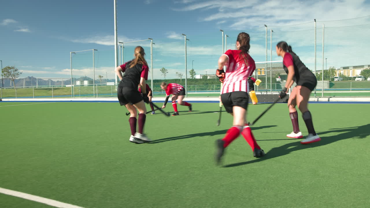 Female hockey players competing intensely on outdoor field under clear sky
