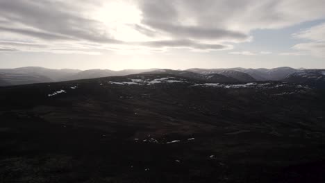 cinematic aerial drone footage rising above a mountain landscape and heather moorland with patches of snow as the sun begins to set behind the clouds