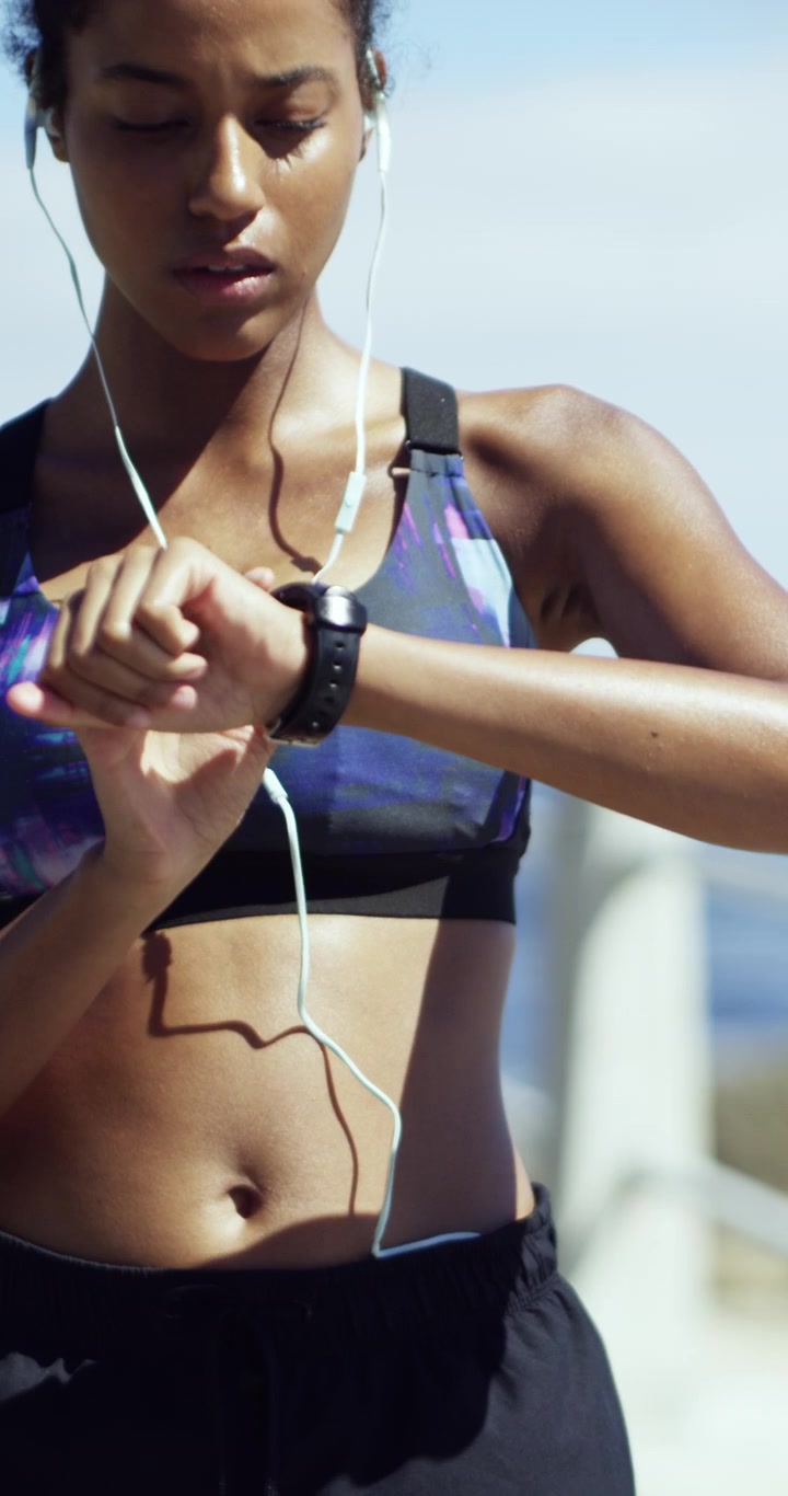 Young Woman Tying Shoelaces and Checking Smartwatch Before Running by the Ocean
