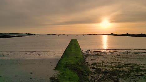 Puesta-De-Sol-Sobre-La-Bahía-De-Cobo-Guernsey-Vuelo-Lento-Sobre-El-Embarcadero-Y-La-Playa-A-Mitad-De-La-Marea-Hacia-El-Atardecer-Con-Barcos-Anclados-Y-Cielo-Dorado