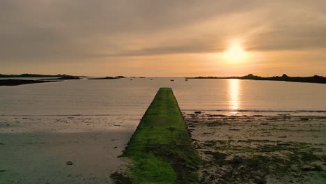 puesta de sol sobre la bahía de cobo guernsey vuelo lento sobre el muelle y la playa a media marea en la puesta de sol con barcos anclados y cielo dorado