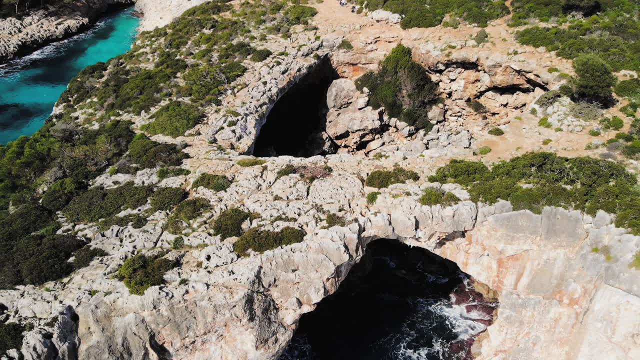 Ripresa aerea con drone in avanti che scende verso un arco naturale sul mare vicino a Cala Varques a Maiorca.