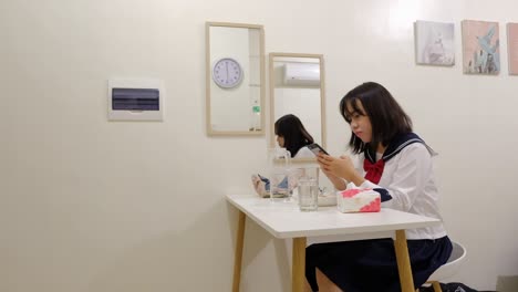 young southeast asian woman in school uniform scrolls on phone at breakfast