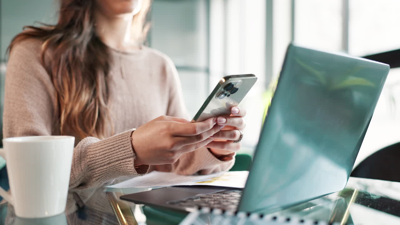 Woman using phone and laptop at desk