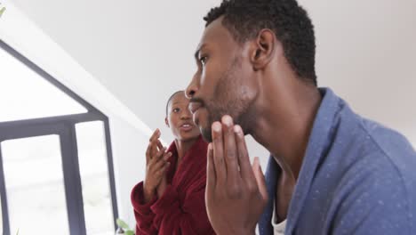 Glückliches-Afroamerikanisches-Paar,-Das-Morgens-Im-Badezimmer-Spricht-Und-In-Den-Spiegel-Schaut,-Zeitlupe