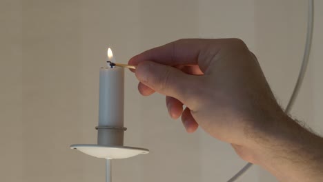 la mano masculina enciende una vela en un soporte colgante con un fósforo, un primer plano slomo