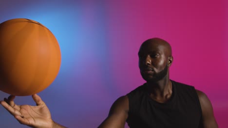 retrato de estudio de un jugador de baloncesto girando la pelota en el dedo contra un fondo iluminado de rosa y azul 2
