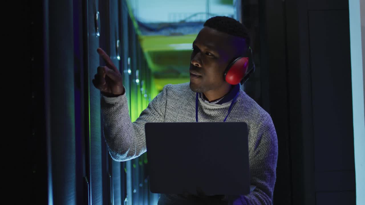 African american male computer technician using laptop working in business server room