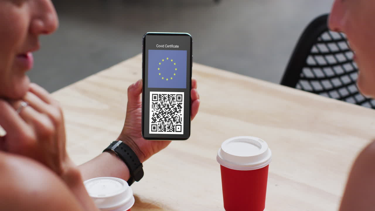 Man at cafe showing smartphone with covid vaccination certificate, eu flag and qr code on screen