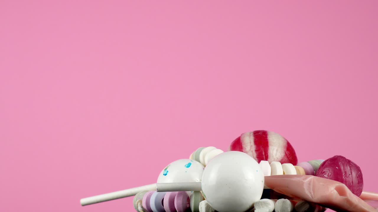 밝은 베이비 핑크 스튜디오 배경에 대해 플래터에서 회전하는 맛있는 모듬 사탕의 일부