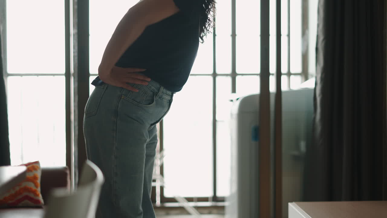A woman standing indoors near a window and a washing machine