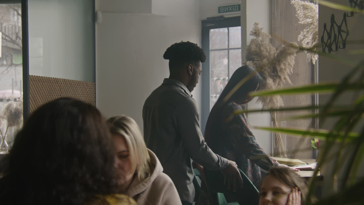 Female Waiter Greets Adult Couple at Entrance Multi Ethnic Couple Coming to Cafe and Smiling Female Waiter Greets Man and Woman at Entrance and Sits People at the Table Diverse Guests in Restaurant with Modern Design Concept of Public Eating