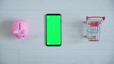 teléfono con una pantalla chromakey en las manos de un primer plano. vista superior de la caja de ahorros del teléfono inteligente y el carrito de compras copia el espacio sobre fondo blanco