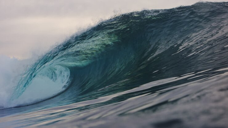 Low ocean surface view of green crystal clear wave barreling in slow motion