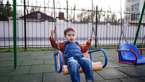 positive caucasian toddler swinging at the playground. baby boy having fun outdoors in autumn.