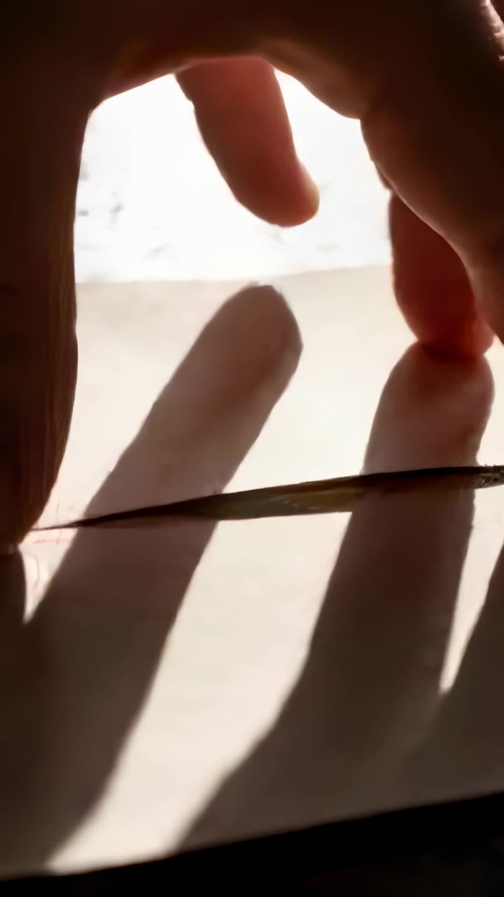 Video verticale: Luce intensa che illumina una singola mano che pizzica un foglio sopra una corda alla finestra, con ombre.