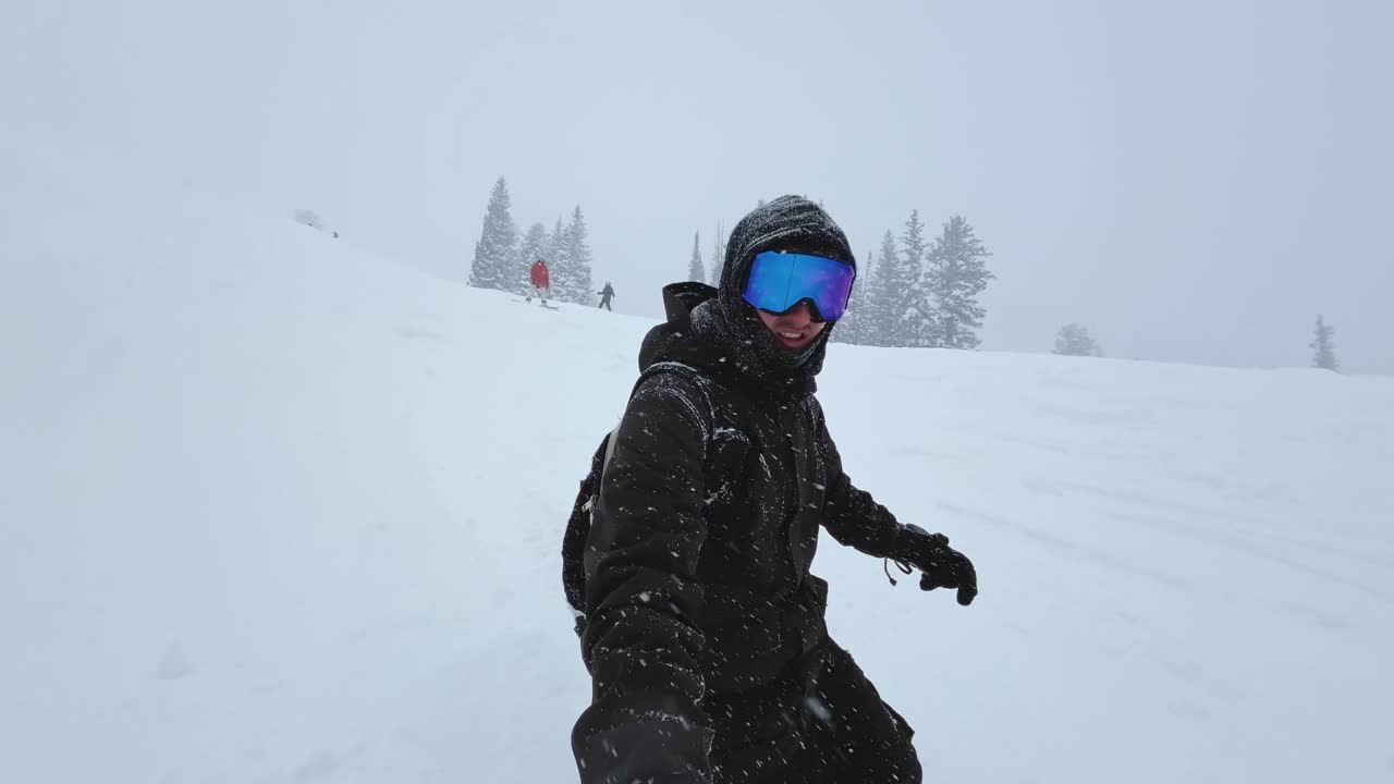 toma de punto de vista portátil de un hombre blanco de unos veinte años vestido con equipo de nieve haciendo snowboard por una colina empinada en una estación de esquí nevada durante una fría tormenta de nieve en las montañas rocosas de utah.