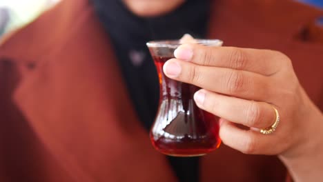 close-up of a woman's hand holding a glass of turkish tea