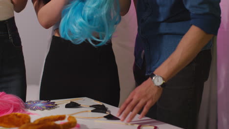 group of friends choosing wigs and props outside photo booth with neon "let's party" sign outside