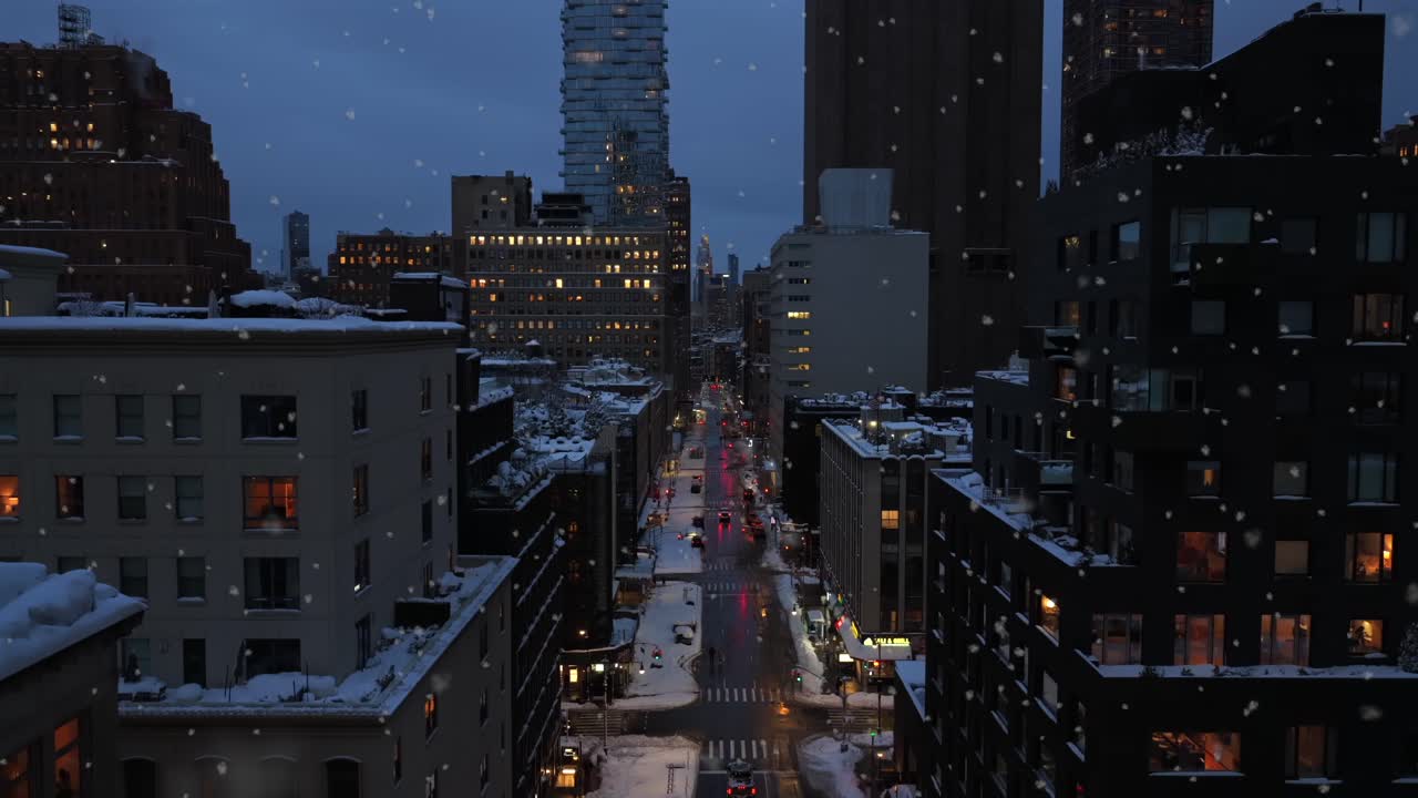 Luftfoto af gade i centrum under snefald i skumringen, med biler, der kører på våde veje mellem bygninger, glødende lys og kold vinterstemning i en amerikansk byscene. Nattescene i USA