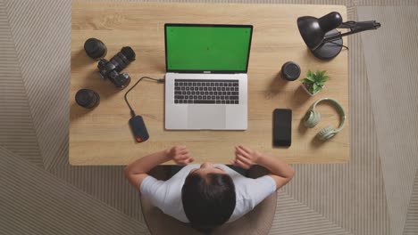 top view of a woman video editor celebrating succeed using green screen laptop and smartphone next to the camera in the workspace at home